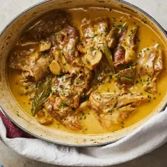 Un plat de lapin à la moutarde crémeuse, garni de persil frais et de champignons, servi dans une cocotte en fonte.