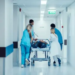 Équipe médicale transportant un patient sur un brancard dans un couloir d'hôpital. Idéal pour une lettre de motivation brancardier sans expérience.