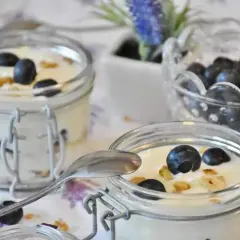 Dwa słoiczki z jogurtem naturalnym, jagodami i granolą. Pyszne śniadanie, które może pomóc w walce z cholesterolem.
