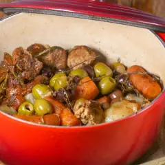 Un savoureux sauté de veau aux olives, carottes et herbes aromatiques mijote dans une cocotte rouge.