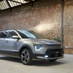 Un Kia Niro gris con detalles rojos en el pilar C, listo para una prueba. El coche está en un interior con paredes de ladrillo y techo acristalado.
