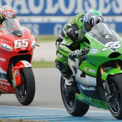 Piloto en moto verde Kawasaki compite en MotoGP, con el número 56. A su lado, otro piloto en rojo Ducati con el 65.