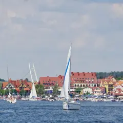 Żaglówki na błękitnych jeziorach na Mazurach, z malowniczym miasteczkiem w tle.