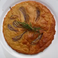 Herzhafte Kichererbsenmehl Rezepte: Goldbrauner Kuchen mit roten Zwiebeln und Rosmarin auf weißem Teller.