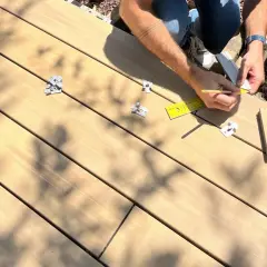 Pose d'une lame composite sur plot. Un artisan mesure avec une règle et un crayon pour une installation précise.