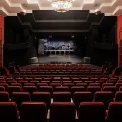 Widownia teatru na Targówku, z rzędami czerwonych foteli i sceną gotową na występ.