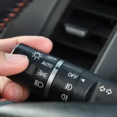 Dłoń manipuluje przełącznikiem świateł w samochodzie, ustawiając go na pozycję "AUTO".