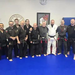 En grupp män i svarta och vita dräkter poserar på en blå matta. De är en del av en kenpo karate-klubb.