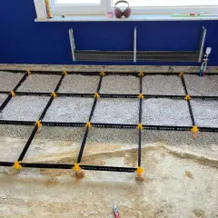 Vorbereitung für **OSB-Platten verlegen**: Ein Boden wird mit Schotter gefüllt und mit einem schwarzen Gitter und gelben Clips für den Trockenestrich vorbereitet.