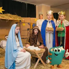 Dzieci w strojach na jasełka odgrywają scenę narodzin Jezusa. Widać Maryję, Józefa, aniołka i trzech króli z darami.
