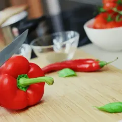 Ręka kroi paprykę czerwoną, bogatą w witaminy. Obok leży chili i pomidory, składniki pełne zdrowotnych właściwości.