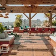 Le perchoir Ménilmontant, un rooftop chic avec vue sur Paris. Canapés confortables, tables dressées, végétation luxuriante et ambiance estivale.