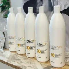 Cinq bouteilles d'oxydant crème universel, dont une de 40 volumes, sont alignées. Ce peroxyde d'hydrogène est enrichi en huile de reine des prés.