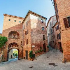 Antica porta in mattoni a Torrita di Siena, con un affresco e un vicolo acciottolato che sale tra case medievali.