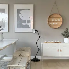 Ein Esszimmer im skandinavischen Stil mit einer warmen grau farbpalette. Ein weißer Tisch, eine Holzbank mit Schaffell und Kunstwerke an der Wand.