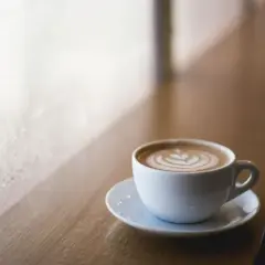 Tazza di cappuccino con latte art su un tavolino di legno, vicino a una finestra appannata. Immagina come mettere le cialde nel portafiltro per un caffè perfetto.