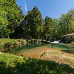Un refrescante pozo do boi con aguas cristalinas, rodeado de exuberante vegetación y una antigua edificación de piedra.