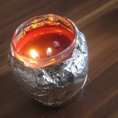 Płonąca świeca w szklanym naczyniu, owiniętym folią aluminiową, tworząc efekt tunelowania świecy.