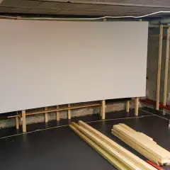 Große, weiße Leinwand für ein Heimkino, gestützt von Holzrahmen. Material für den **Beamer Leinwand selber bauen** liegt bereit.