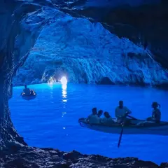 Barche a remi navigano nelle magiche grotte blu, illuminate da una luce surreale che rende l'acqua di un blu intenso.