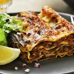 En saftig bit lasagne med köttfärs och ost, serverad med en fräsch sallad och citronklyfta. Perfekt för lasagnens dag!