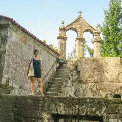 Mujer posa frente a la entrada del monasterio de San Pedro de Rocas, con su arquitectura de piedra y escalinata antigua.