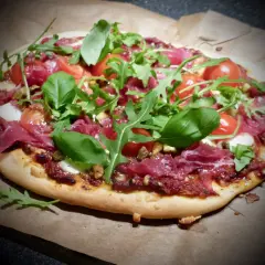 En läcker bresaola pizza med tomater, ruccola och färsk basilika.