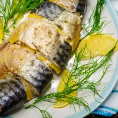 Pieczona makrela z cytryną i koperkiem na talerzu, gotowa do podania z niebieskimi sztućcami.