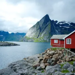Två röda stugor vid en sjö i Norge, med dramatiska berg i bakgrunden. Perfekt för en vandring i Norge.