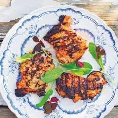 Grillad yoghurtmarinerad kyckling med gröna blad och klöver på en blåvit tallrik.