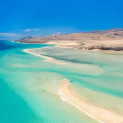 Aguas turquesas y arena dorada en Fuerteventura. Un paraíso natural para descubrir qué ver en Fuerteventura, con montañas áridas al fondo.