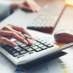 Dłoń z długopisem naciska klawisze kalkulatora, obok klawiatura i myszka. Analiza finansowa dla BNP Paribas Leasing.