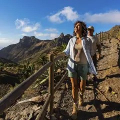 Ett par njuter av en vacker la gomera vandring i solsken, med dramatiska berg och palmer i bakgrunden.