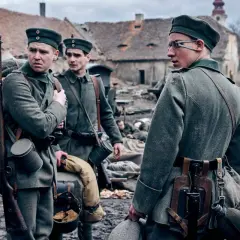 Żołnierze w mundurach z I wojny światowej, z karabinami i plecakami, stoją na błotnistym podwórzu. Na zachodzie bez zmian obsada.