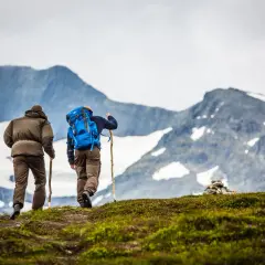 Två vandrare på väg mot Storulvån, kanske efter en bussresa från Duved. Majestätiska berg i bakgrunden.
