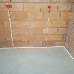 Przewody w posadzce bez peszla, przygotowane do dalszych prac instalacyjnych. Widoczne puszki instalacyjne w ścianie z cegły.