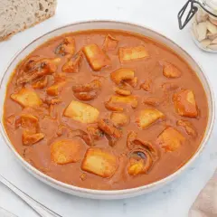 Un plato humeante de jibia en salsa, con trozos de patata y pan rústico al lado.