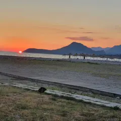 Zachód słońca nad morzem w Czarnogórze w czerwcu. Idealna pogoda na plażowanie, z górami w tle i rzędem parasoli.