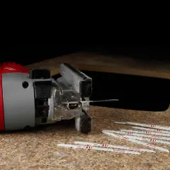 Scie sauteuse rouge et grise, prête à découper. Lames neuves à proximité, prêtes pour le mouvement pendulaire.
