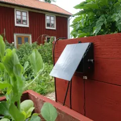 En solcellsdriven bevattning sköter om växterna vid ett rött hus.