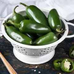Świeże, zielone papryczki **jalapeno** w durszlaku, gotowe do przygotowania pikantnych potraw. Kilka przekrojonych sztuk pokazuje ich wnętrze.