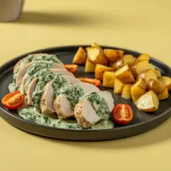 Pokrojona pierś z kurczaka ze szpinakiem w sosie śmietanowym, podana z pieczonymi ziemniakami i pomidorkami koktajlowymi.