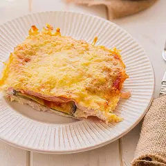 Porción de pastel de berenjenas gratinado con queso dorado, servido en plato blanco.