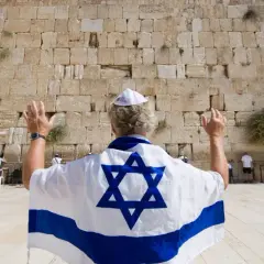 Mann mit israelischer Flagge und Davidstern betet an der Klagemauer, ein Ort des Judentums in Israel.