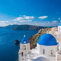 Santorini, idealne miejsce, gdzie na wakacje w sierpniu. Białe domy z niebieskimi kopułami nad turkusowym morzem.