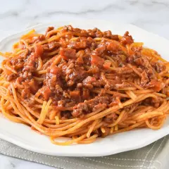 Un plato de espaguetis con carne picada, cubierto con una rica salsa de tomate y trozos de carne.
