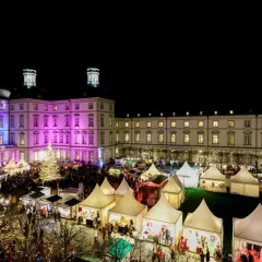 Festlicher weihnachtsmarkt schloss bensberg mit beleuchtetem Baum, bunten Lichtern und vielen Besuchern in Zelten.