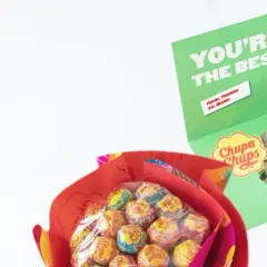 En person håller upp ett kort med texten "YOU'RE THE BEST" och en bild på sig själv. Bredvid syns en bukett med Chupa Chups-klubbor, en fin godis present diy.