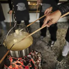 Des morceaux de pain trempent dans un caquelon de fondu suisse fumant, chauffé au-dessus d'un feu de bois.