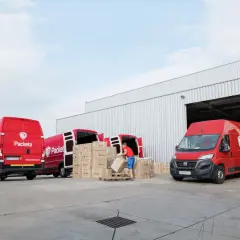 Pracownik rozładowuje paczki z czerwonego busa Packeta. Awizacja dostawy w magazynie.